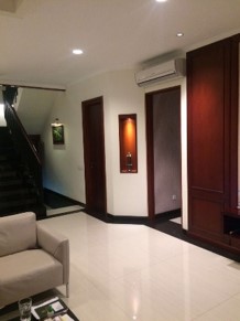 Ruang keluarga rumah di Kelapa Gading dengan tangga, lantai marmer, dan panel kayu gelap