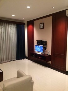 Ruang televisi rumah di Kelapa Gading dengan kabinet kayu dan jendela bertirai