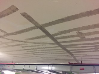 Langit-langit beton bercat putih di The Energy Building dengan jalur-jalur permukaan yang dikupas membentuk pola menyilang